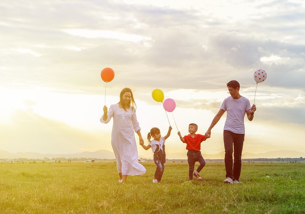 Familia caminando en el campo con globos en la mano fondo de atardecer