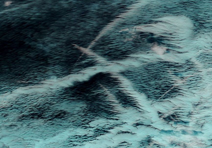 Imagen RGB del sensor MODIS del satélite TERRA al mediodía del 23 de febrero de 2012. La imagen es realzada de tal manera que las nubes con topes formadas por gotitas de agua se presentan en blanco, y las formadas por cristalitos de hielo en cián. Nótese como una misma estela de barco pasa del blanco al cián denotando un cambio de fase en sus topes.