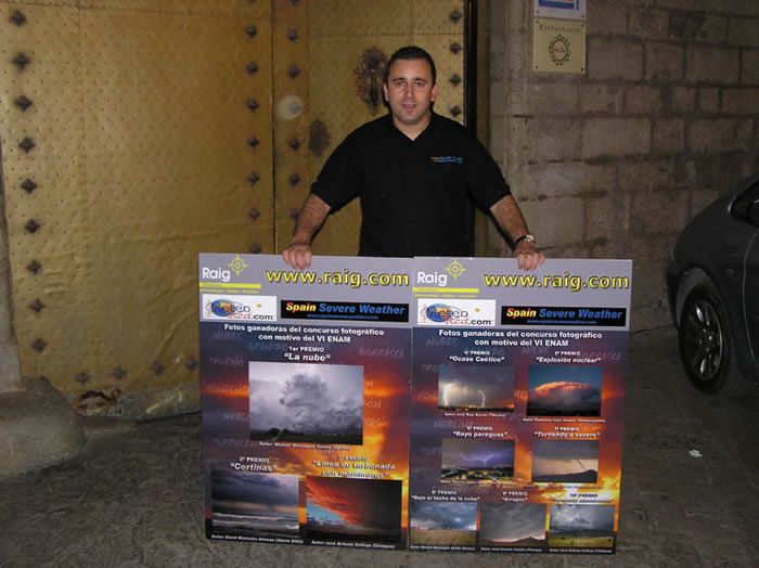 Alberto Lunas sostiene los carteles de las fotos ganadoras patrocinadas por RAIG, SSW y Meteored
