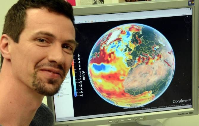 Figura 2.- Roelof Rietbroek junto a una pantalla de ordenador en la que se muestra una imagen del aumento global del nivel del mar. Los diversos colores representan niveles diferentes. Fotografía de Johanne Seiler/Universidad de Bonn.