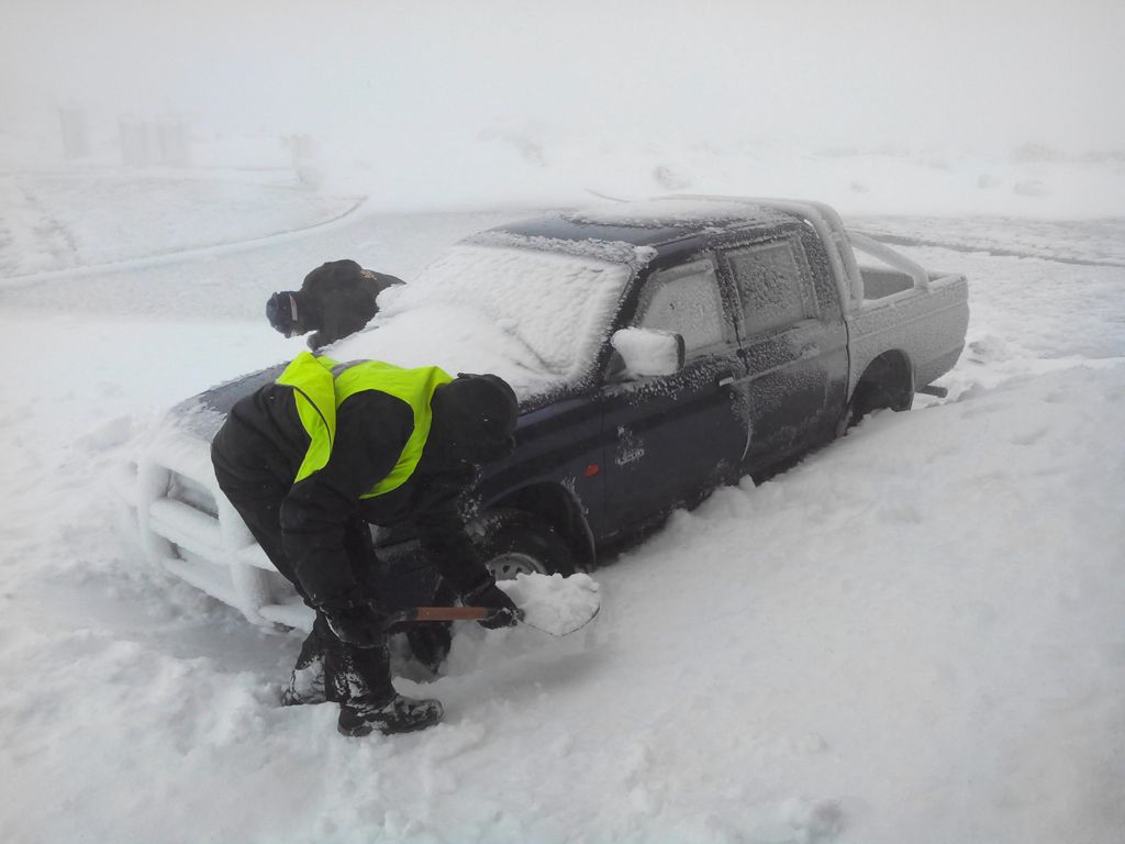 Personal del Observatorio de Izaña se afana en retirar la nieve que ha sepultado las ruedas de un vehículo todoterreno.