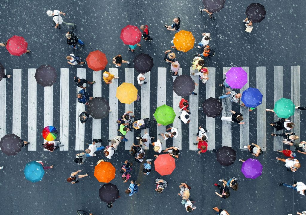 Personas cruzando un paso de peatonal, con paraguas, en día de lluvia, vistas desde encima