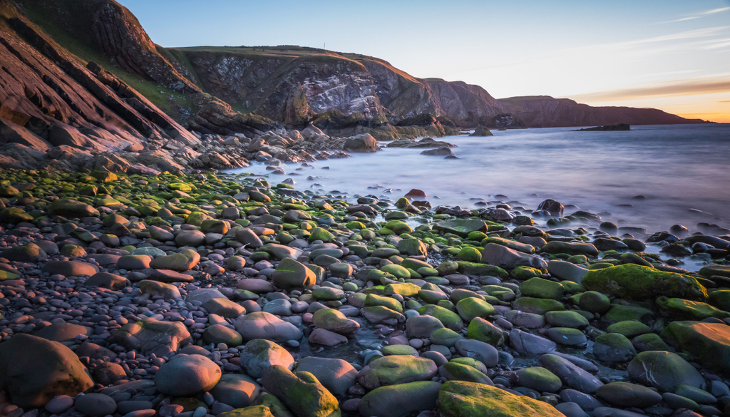 O pôr do sol na Baía de Pettico Wick, St Abbs, Escócia junto da falésia.