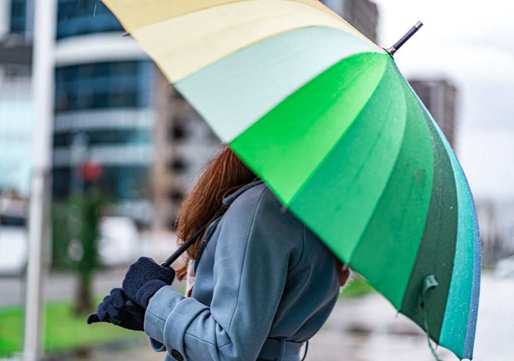 mujer afirmando con sus manos un paraguas verde abierto mujer afirmando con sus manos un paraguas verde abierto