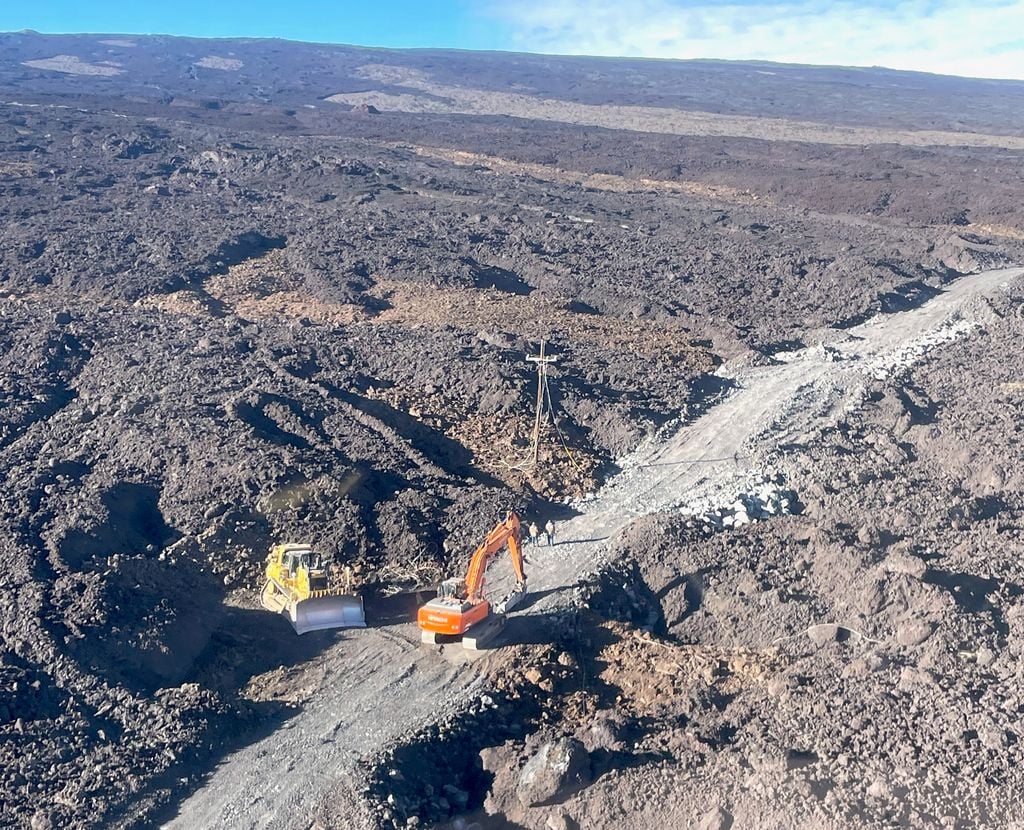 Vista aérea de un equipo de trabajadores construyendo una carretera provisional a través de los flujos de lava solidificada tras la erupción del volcán Mauna Loa en 2022. Un equipo de construcción vial establece una base provisional para la carretera a lo largo de 1,9 kilómetros de flujos de lava provenientes de la erupción del volcán Mauna Loa en 2022. Esta fotografía fue tomada el 3 de marzo de 2026, durante un proyecto para restablecer el acceso al Observatorio Mauna Loa de la NOAA. La carretera se completó el 26 de marzo de 2026. (Crédito de la imagen: Christine Smith/NOAA)