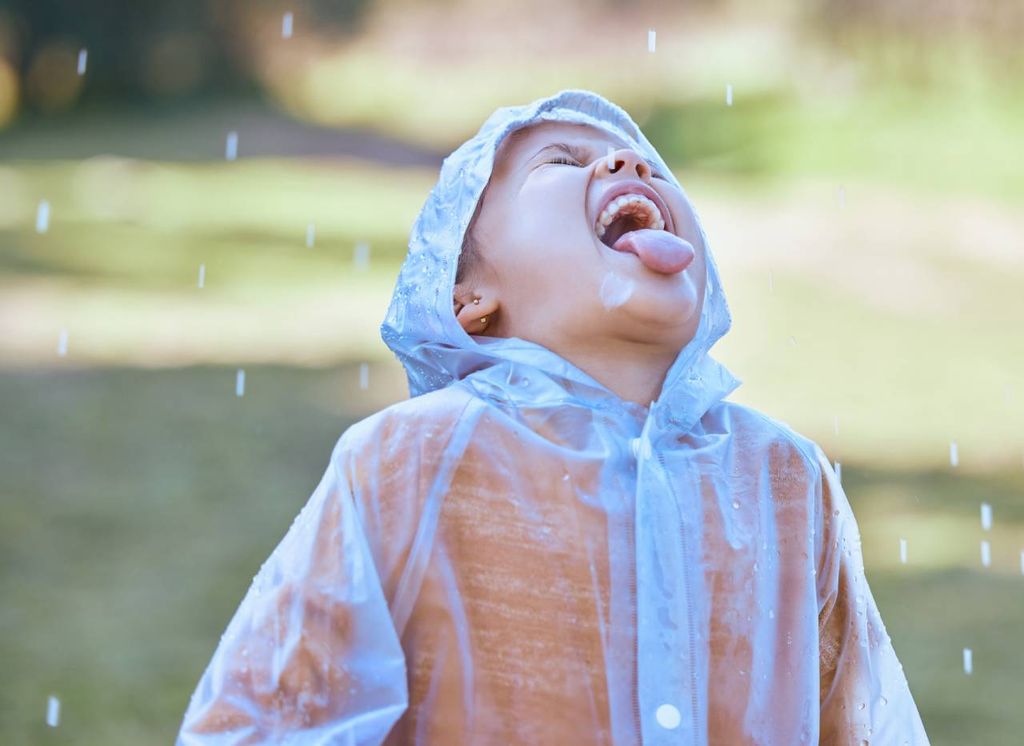 niño con la boca abierta apuntada al cielo para beber agua de la lluvia