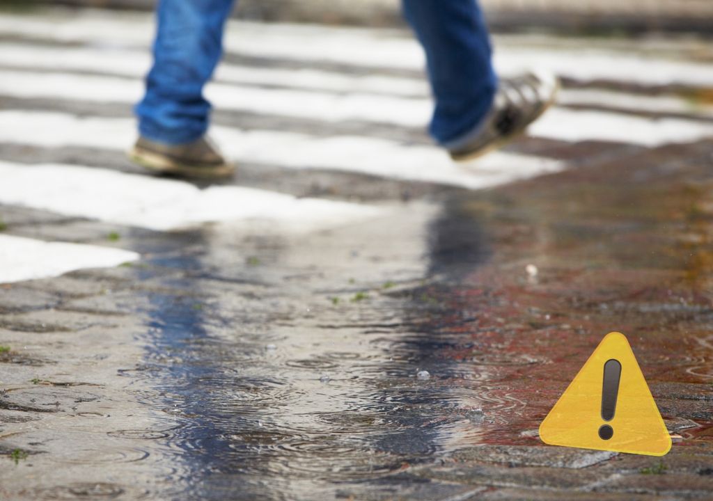 persona cruzando por un paso peatonal en un calle mojada por la lluvia
