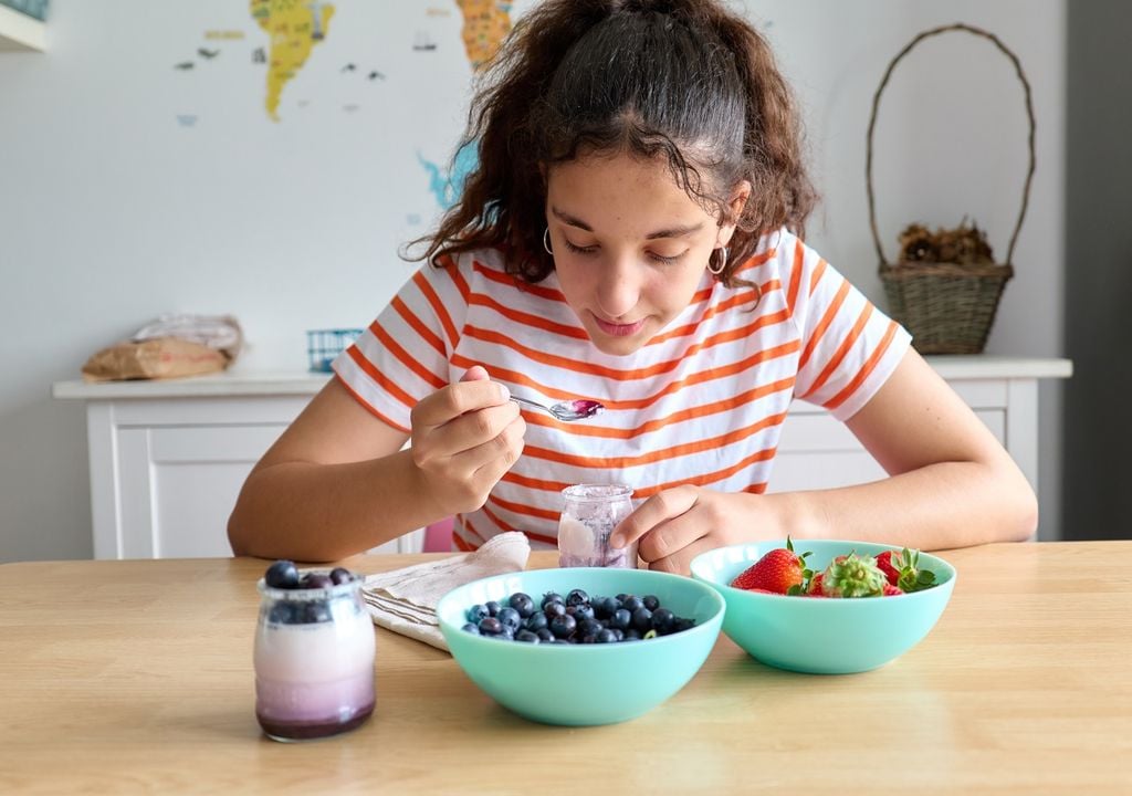 Mujer joven comiendo desayuno con bayas, frutillas y yogurt