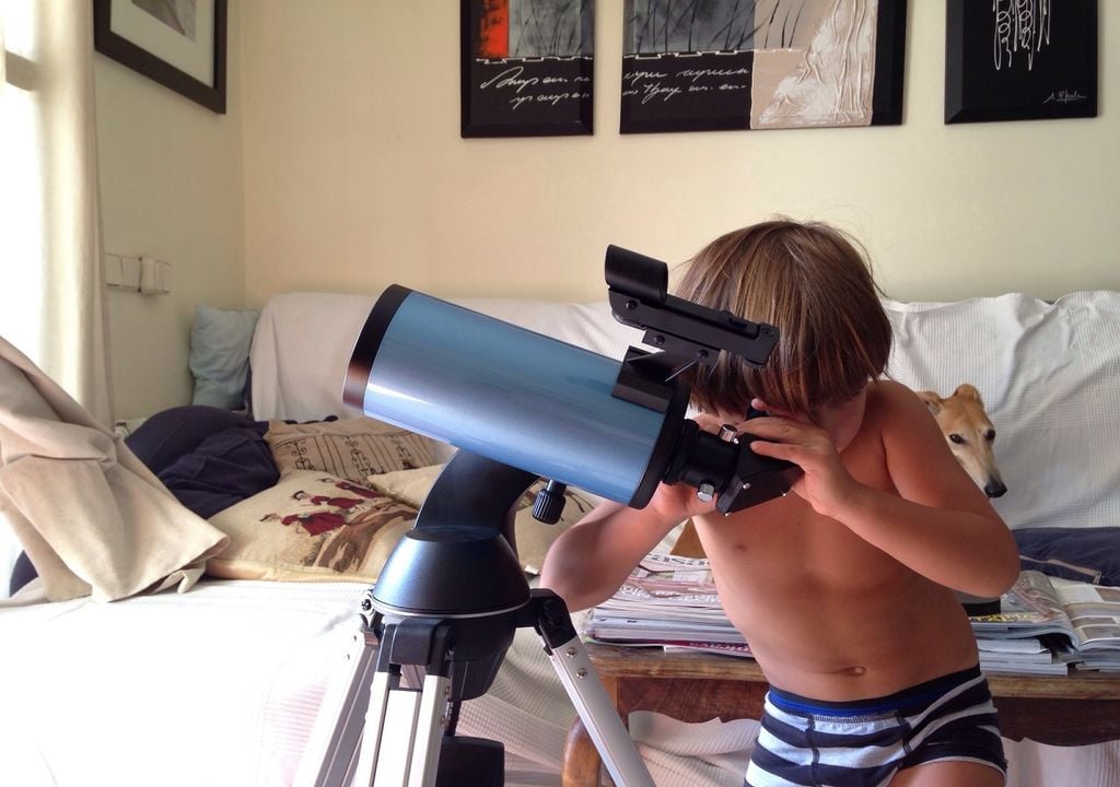 Niño mirando las estrellas con un telescopio en casa.