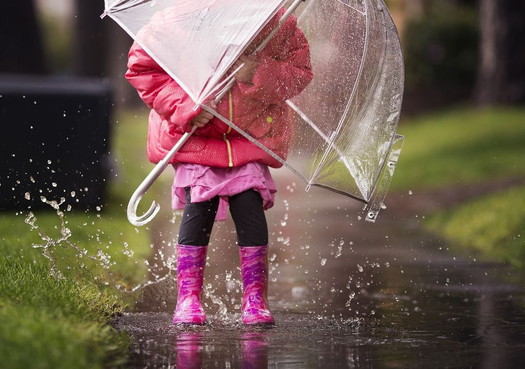 niña con paraguas jugando en el agua