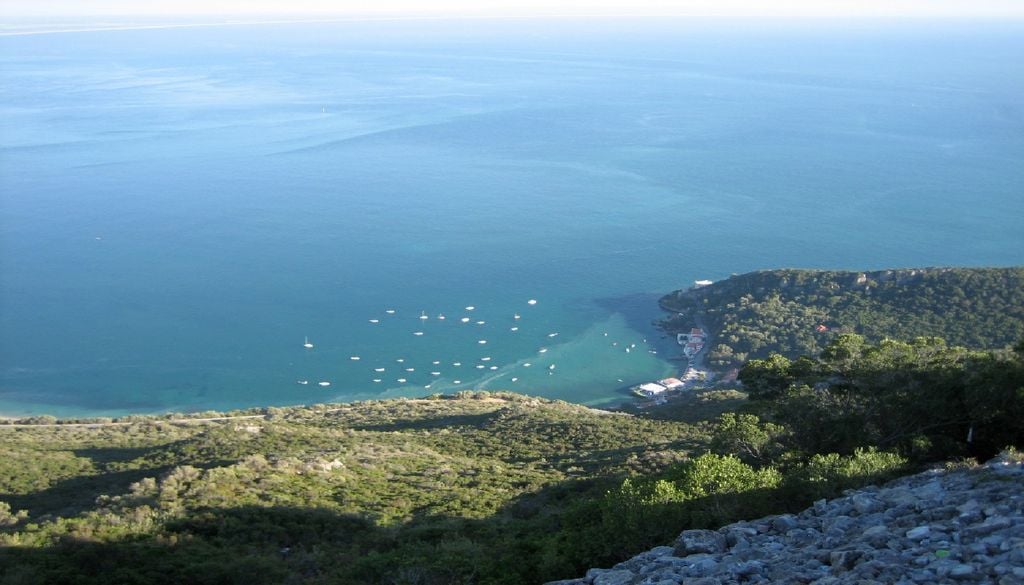 Portinho da Arrábida, Setúbal Disposta numa enseada em meia-lua e protegida da nortada pela serra, a praia do Portinho da Arrábida é uma das estâncias mais visitadas no verão. Foto: Bosc d'Anjou, CC BY 2.0, via Wikimedia Commons