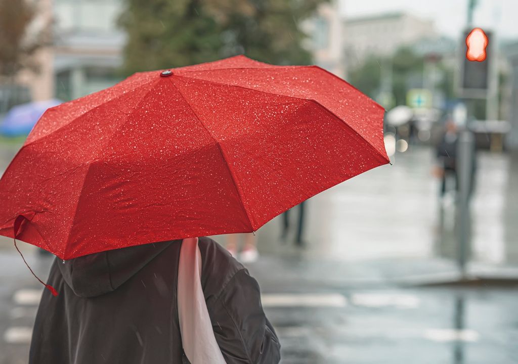 persona con paraguas, bajo la lluvia, esperando en la calle frente a un semáforo en rojo