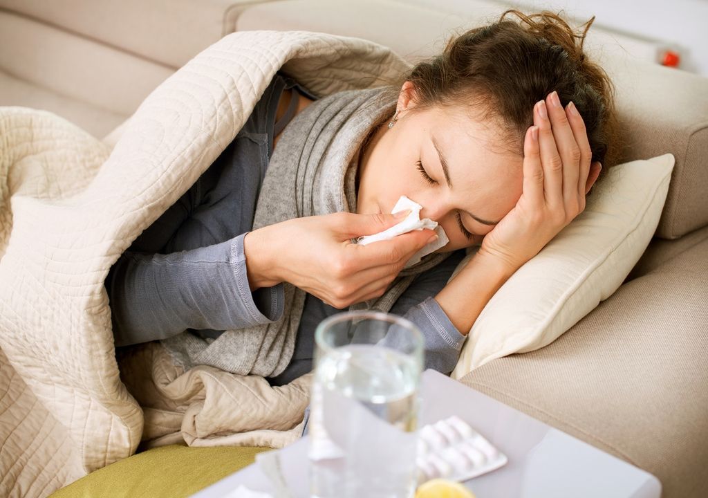 Mujer enferma recostada en sofa y mesa con antibióticos