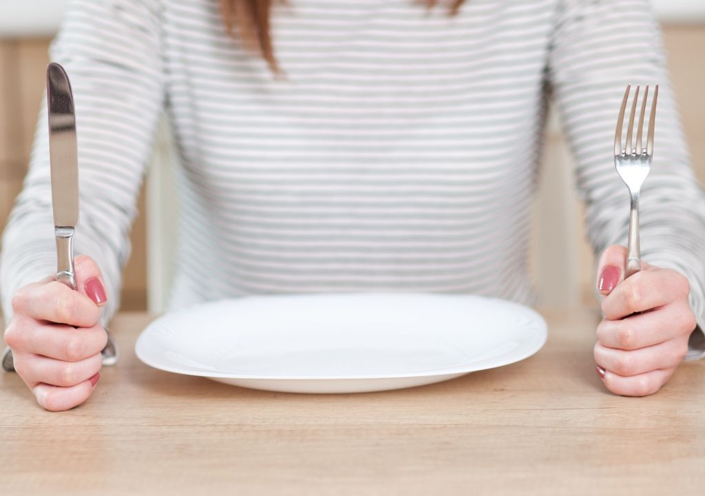 persona frente a un plato vacía, afirmando un tenedor y un cuchillo en sus manos