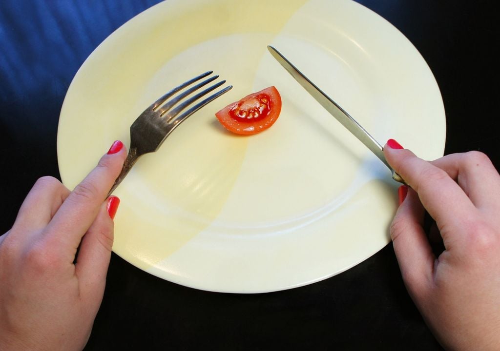 plato con un pequeño pedazo de tomate y una persona sosteniendo un tenedor y cuchillo para comer plato con un pequeño pedazo de tomate y una persona sosteniendo un tenedor y cuchillo para comer
