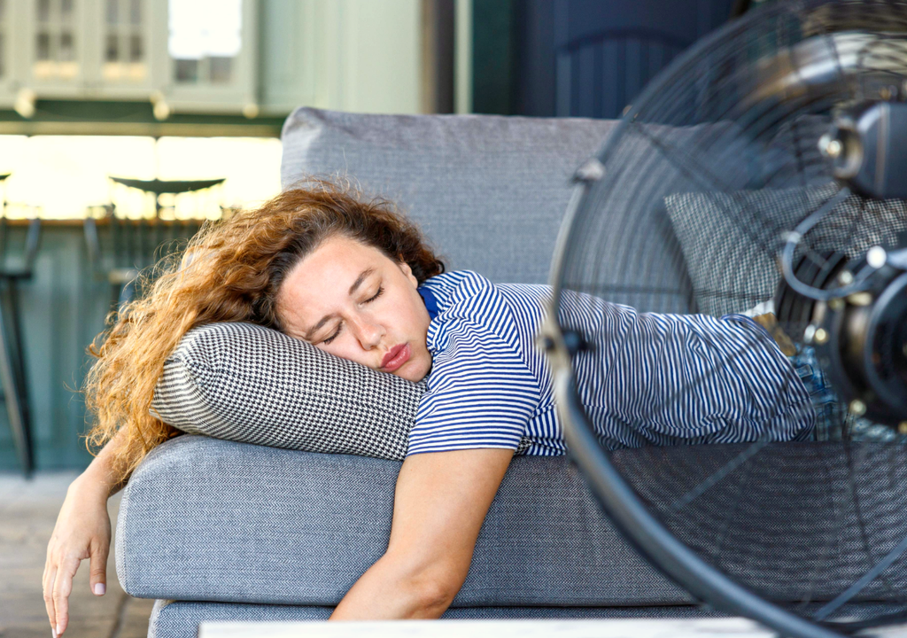 persona durmiendo en el sofá, con un ventilador de aire cerca