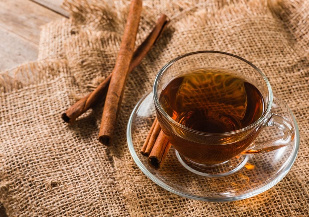 Cup of tea with cinnamon on rustic tablecloth and wooden table