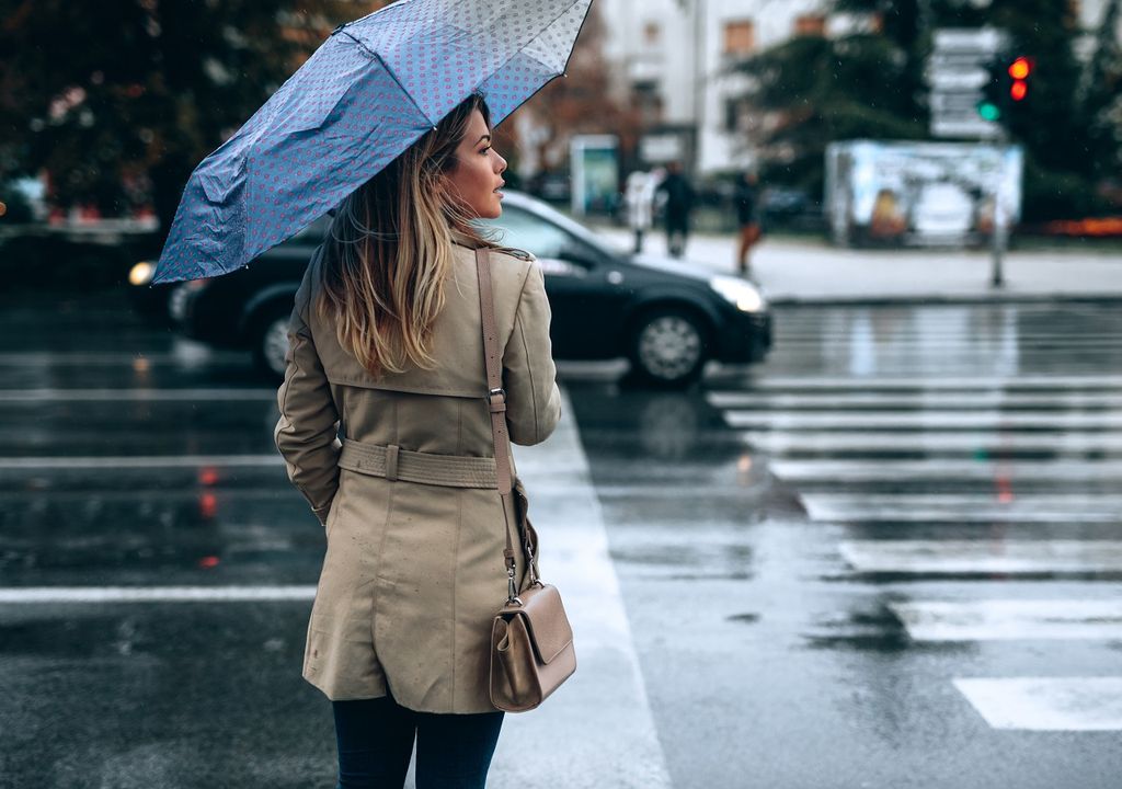 Persona con paraguas esperando para atravesar la calle
