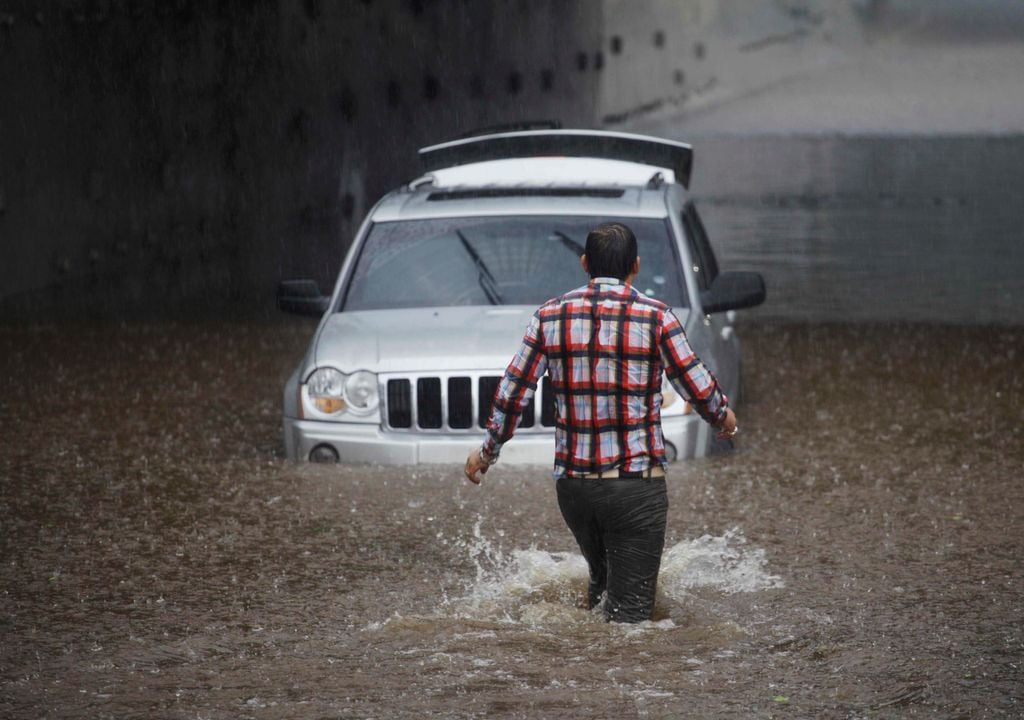 Imagem de homem e veículo enfrentando um alagamento em zona urbana.