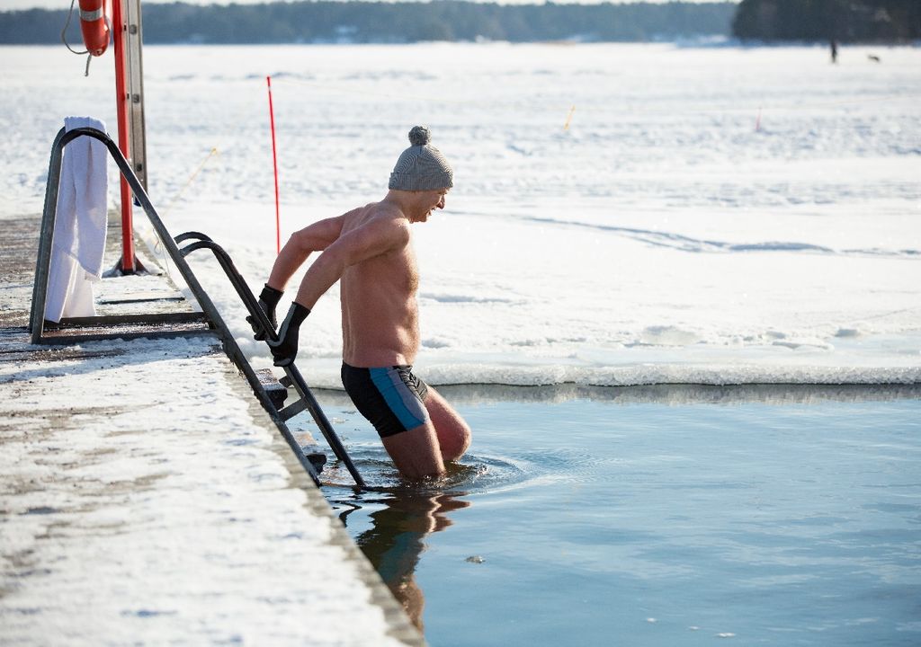 Hombre con traje de baño ingresando a una piscina con agua gélida en medio de la nieve Hombre con traje de baño ingresando a una piscina con agua gélida en medio de la nieve