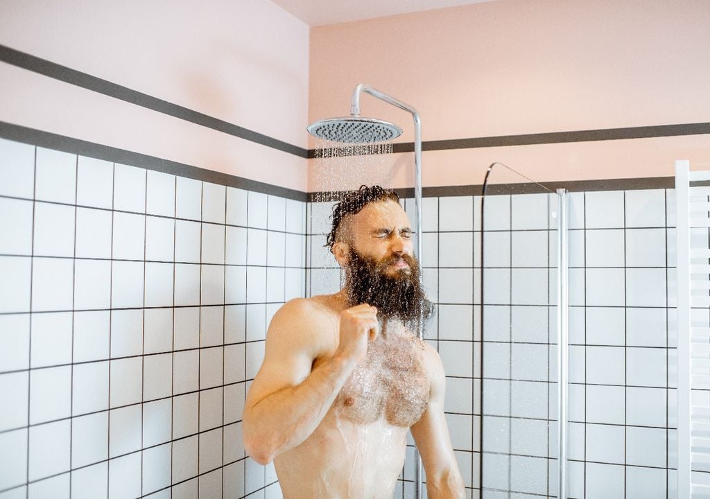 Hombre tomando ducha fría, paredes de cerámica, baño