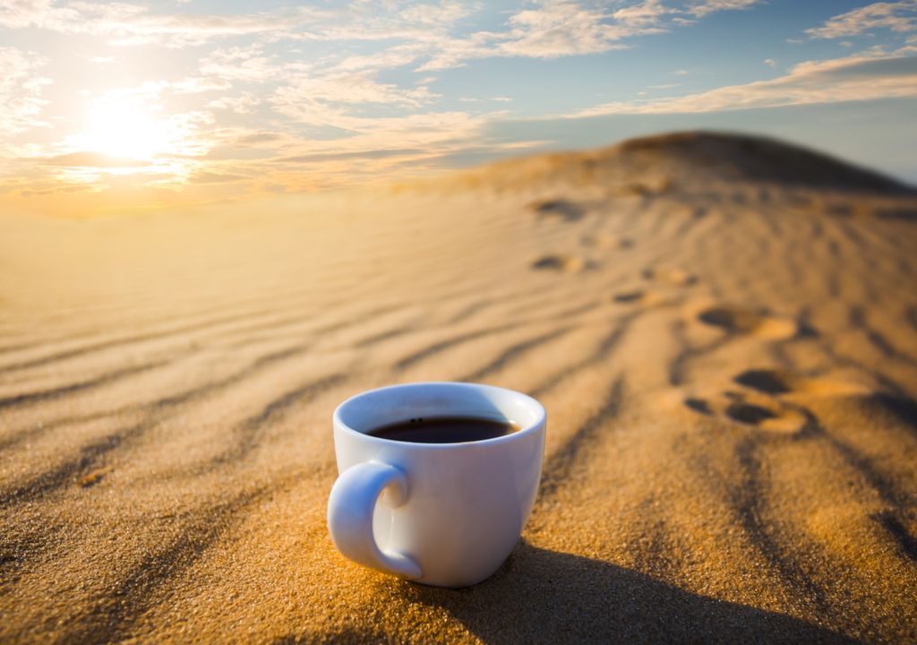 taza de café en medio de la arena y Sol alto en el cielo