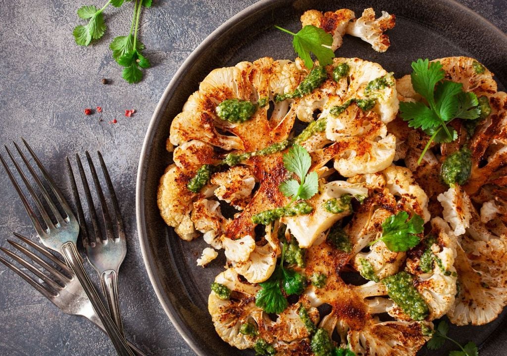 Coliflor asada con especias en plato oscuro, tenedores lado izquierso, Meteored Chile Coliflor asada con especias en plato oscuro, tenedores lado izquierso, Meteored Chile