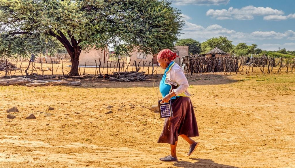 Una donna in un villaggio africano, con un pannello fotovoltaico portatile
