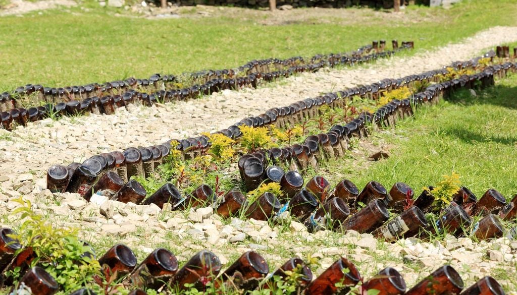 Las botellas de vidrio de tonos verdes o ámbar se pueden reutilizar para delimitar caminos y aportar color al jardín durante el invierno.