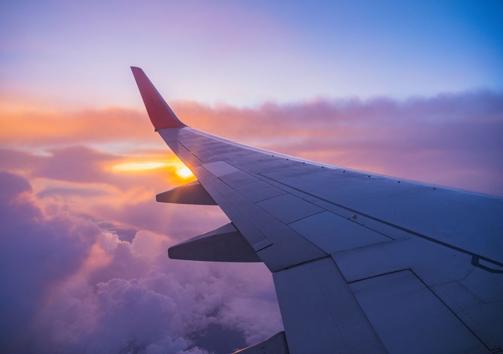 Vista de una ala de avión que vuela sobre las nubes con el Sol en el horizonte