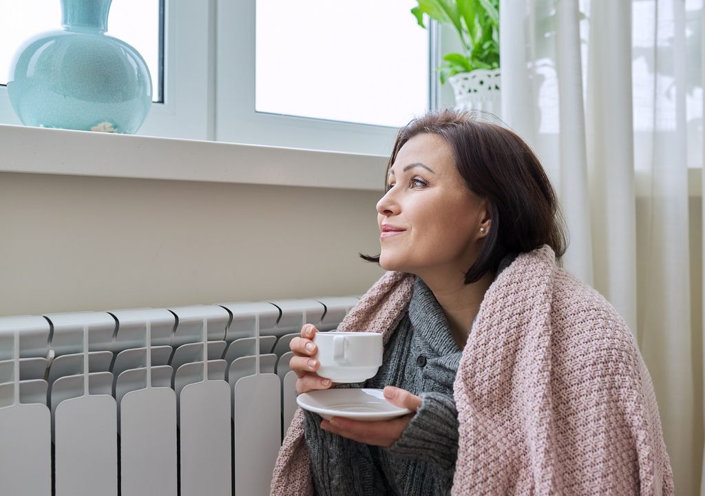Mujer tomando café costado de ventana lado de estufa