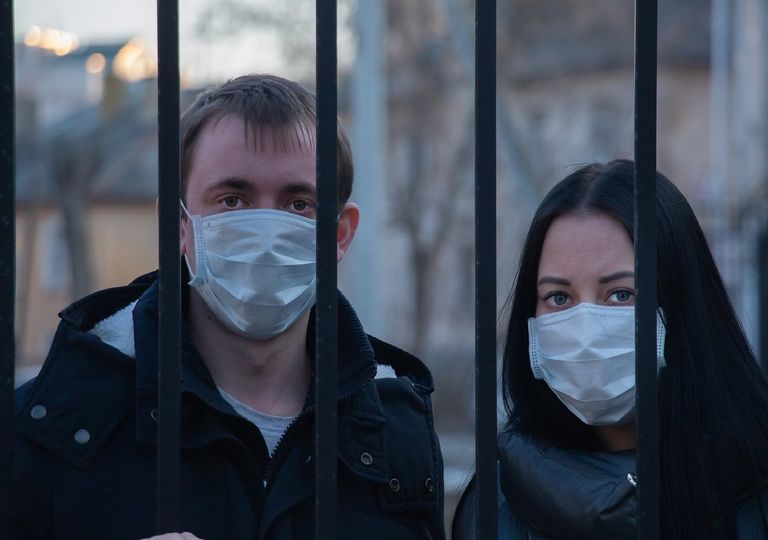 Dos personas con máscaras detrás de una reja Dos personas con máscaras detrás de una reja