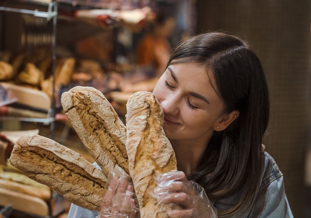Mujer oliendo pan baguette en un supermercado