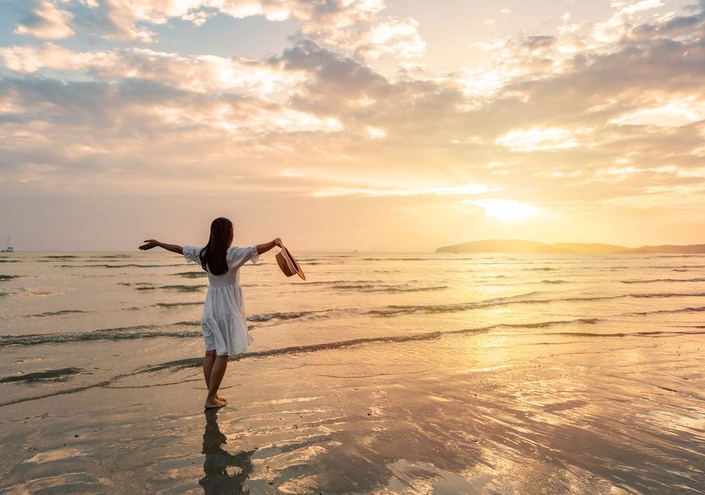 persona con los brazos abiertos hacia el sol, en una playa