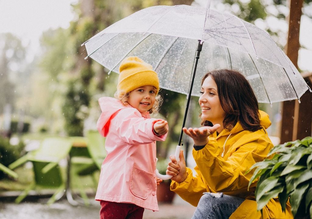 una mujer adulta y una niña pequeña bajo un paraguas en día de lluvia