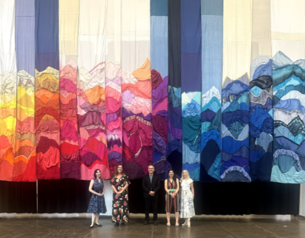 Parte del equipo de “De Atacama a Helsinki” frente a la instalación textil de gran formato exhibida en la Bienal BELA 2025. La obra, confeccionada con ropa en desuso, representa los paisajes del altiplano chileno y fue reconocida como una de las más impactantes del evento. Parte del equipo de “De Atacama a Helsinki” frente a la instalación textil de gran formato exhibida en la Bienal BELA 2025. La obra, confeccionada con ropa en desuso, representa los paisajes del altiplano chileno y fue reconocida como una de las más impactantes del evento.