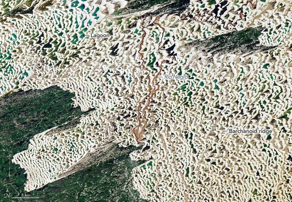 En esta vista de una parte del campo de dunas, se aprecian mejor los distintos tonos azules y verdes de las lagunas. Un pequeño río de aguas marrones discurre hacia el norte a través del campo de dunas. Los vientos que soplaban del noreste crearon las líneas de dunas visibles en esta vista detallada de una parte de la imagen Landsat 9 que se muestra arriba. NASA Earth Observatory/Michala Garrison