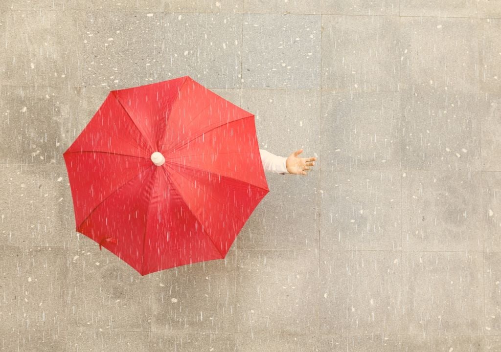 persona extendiendo la mano bajo un paraguas para sentir la lluvia