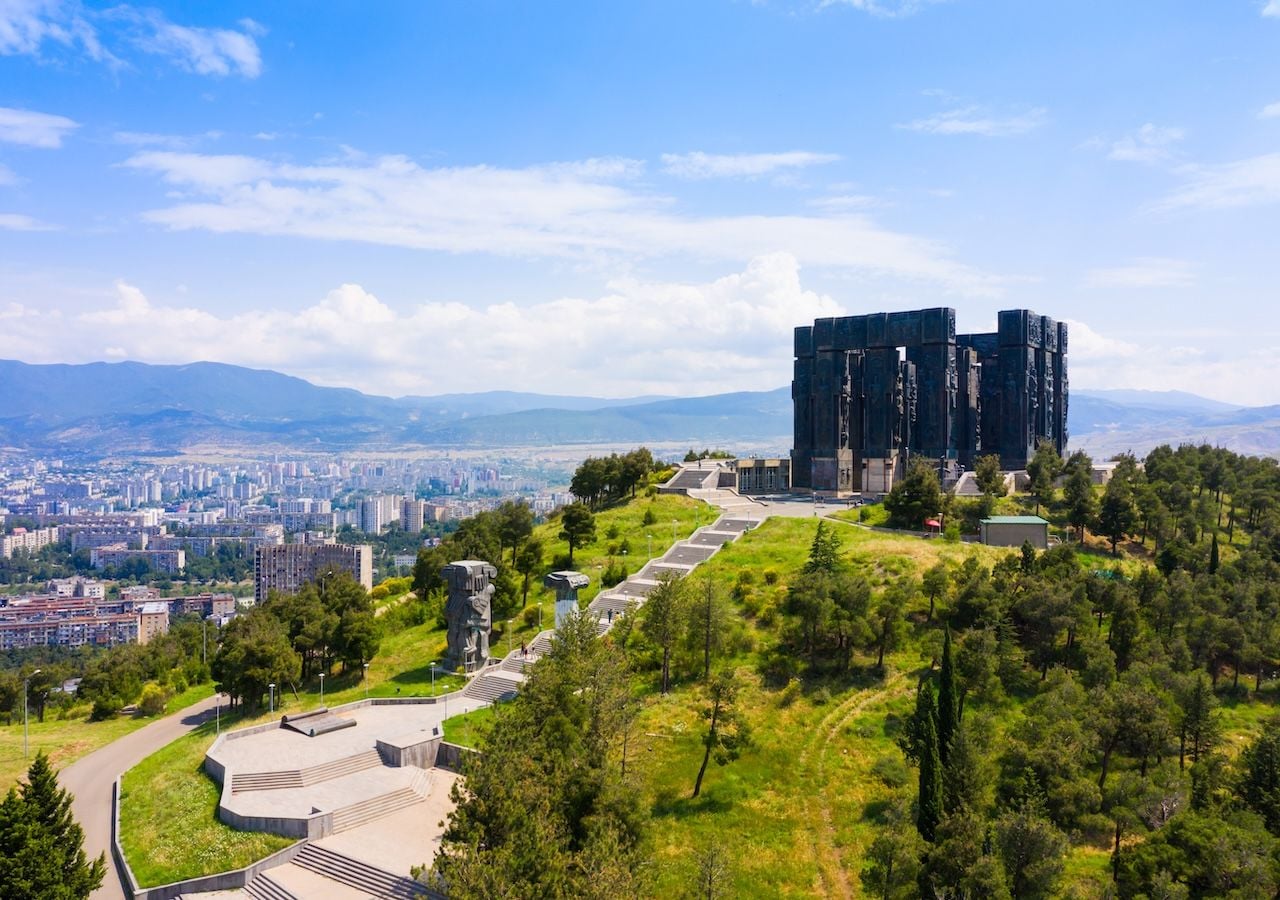 Este monumento se alza a más de 700 metros de altitud y es visible desde distintos puntos de Tiflis. Su emplazamiento conecta con antiguos caminos de peregrinación, y su ubicación fue elegida por su fuerte carga simbólica.