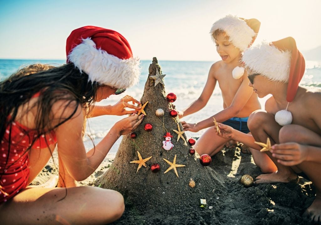 niños y niñas decorando un árbol de navidad de arena en la playa