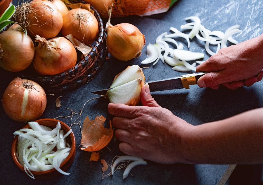 Persona cortando cebolla sobre mesa con más cebollas