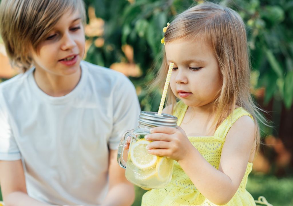 Niña con limonada en sus manos acompañada de su hermano mayor fondo de jardín
