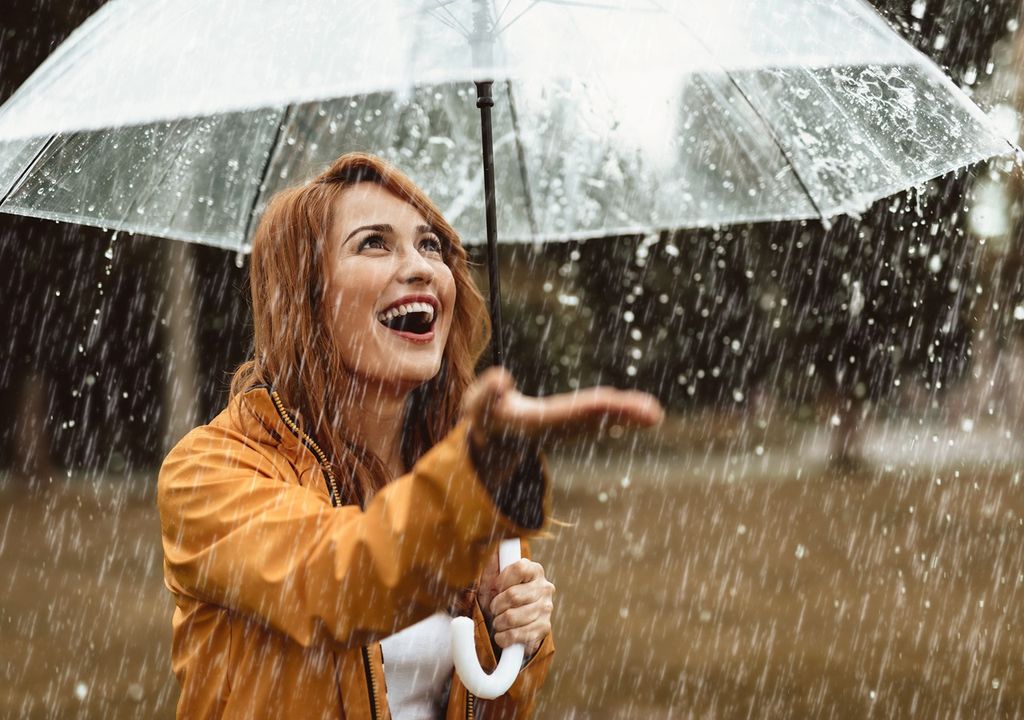 mujer con un paraguas protegiéndose de la lluvia y con una mano estirada para alcanzar las gotas que caen