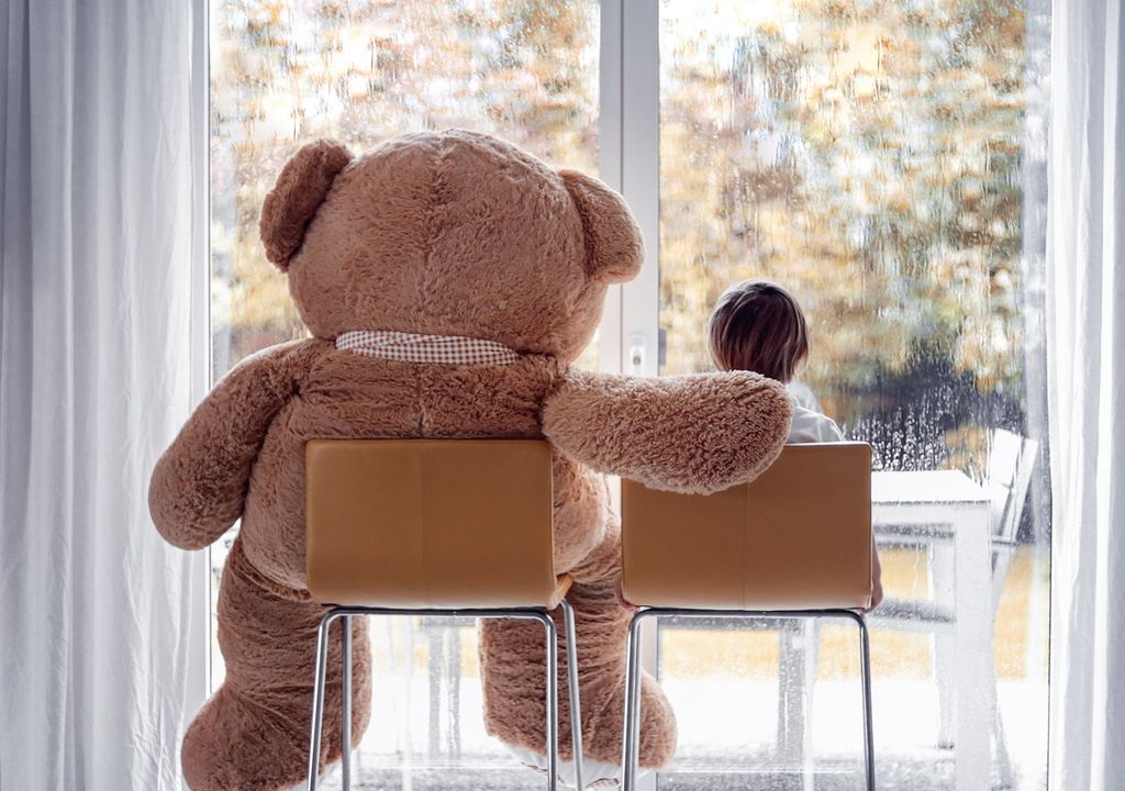 Niño y su amigo oso viendo caer la lluvia por la ventana