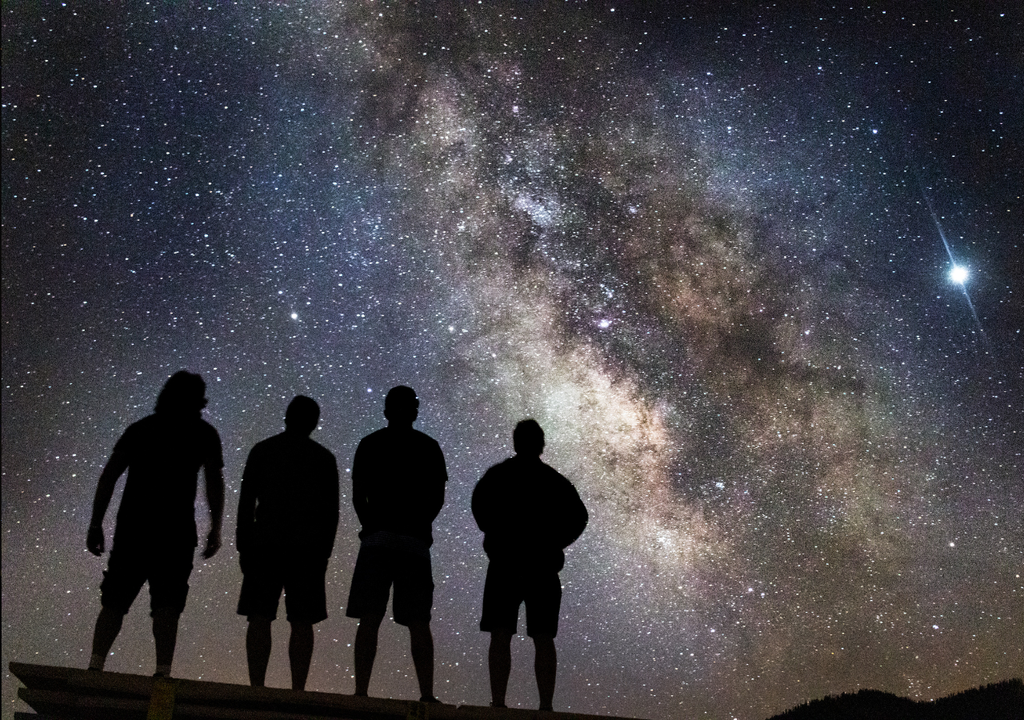Bajo la Vía Láctea, cuatro observadores contemplan cómo el cielo revela el ciclo de vida y muerte de las estrellas