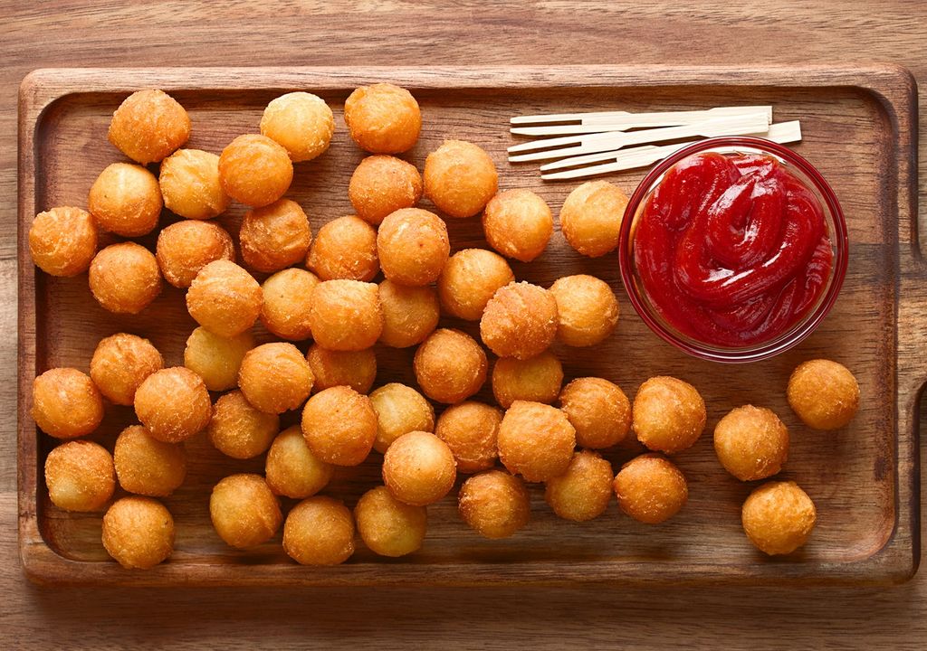 papas duquesas en una tabla para picar, acompañadas de un pote de salsa