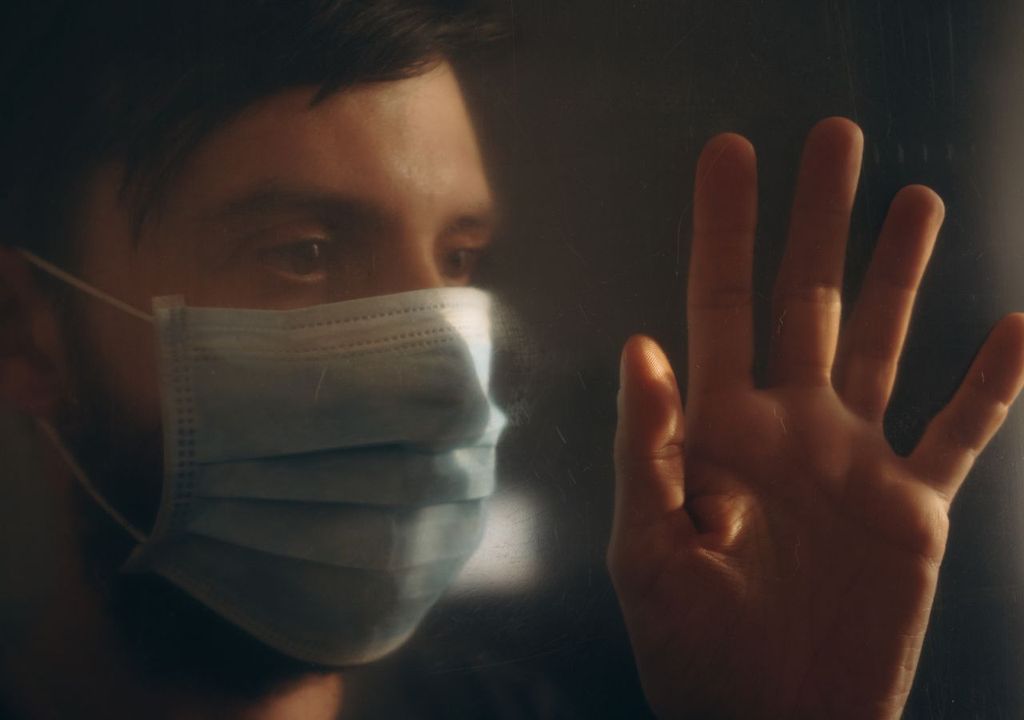 Hombre con mascarilla tras una ventana, fondo negro