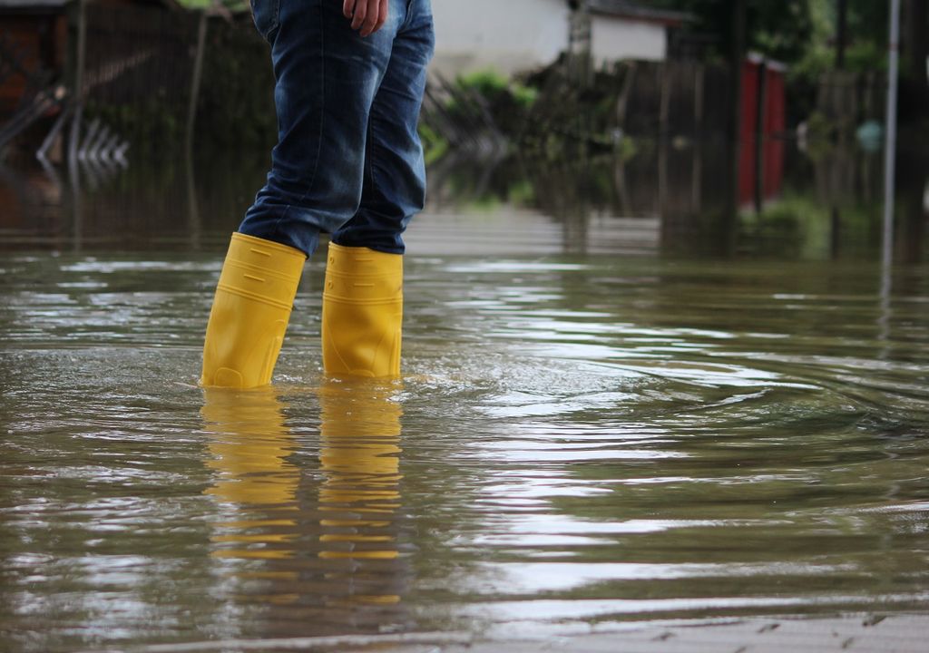 Inundación, persona con botas amarillas, fondo casa.