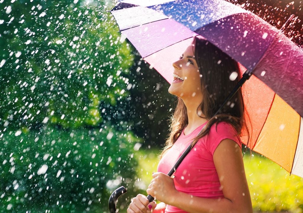 persona feliz con un paraguas y usando ropa veraniega, protegiéndose de la lluvia