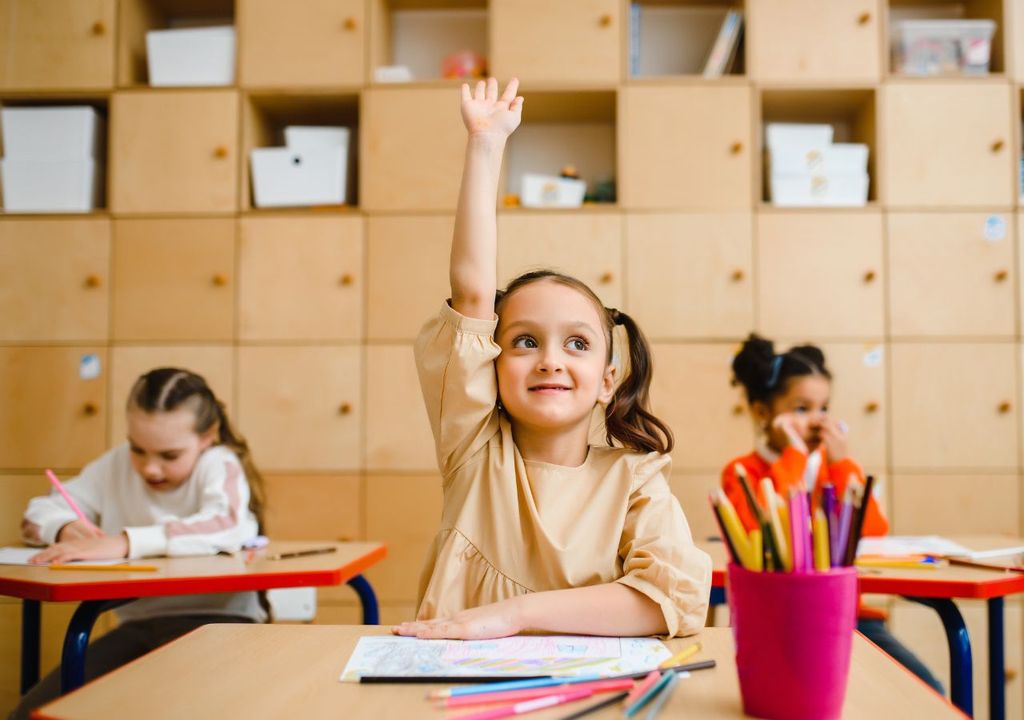 Niña levantando la mano en sala de clases junto a dos compañeras de curso.